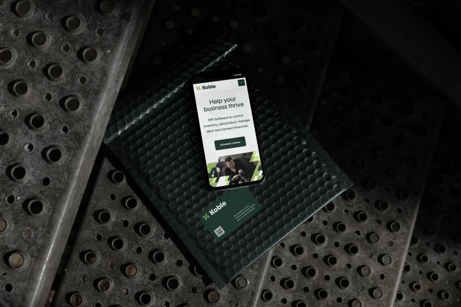 The Koble mobile website and business card on an industrial surface.